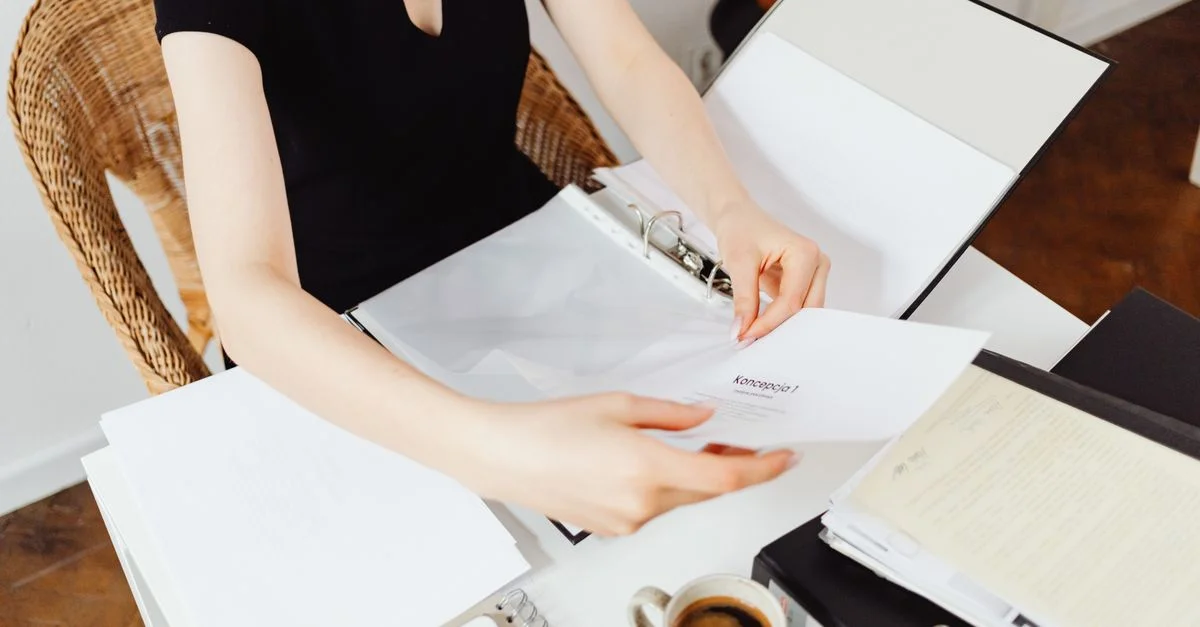 Une femme assise à un bureau organisant des documents dans un cadre de bureau avec une tasse de café et un smartphone à proximité.