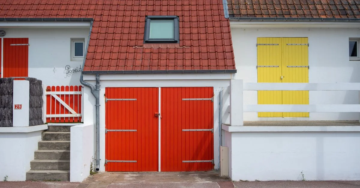 Façade de maison aux couleurs vives, avec des portes rouges et jaunes et un toit de tuiles rouges.