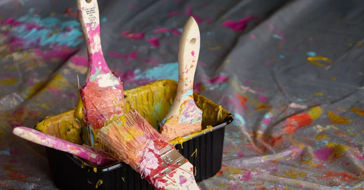 Des pinceaux vibrants recouverts de peinture dans un plateau sur un fond de toile éclaboussé.